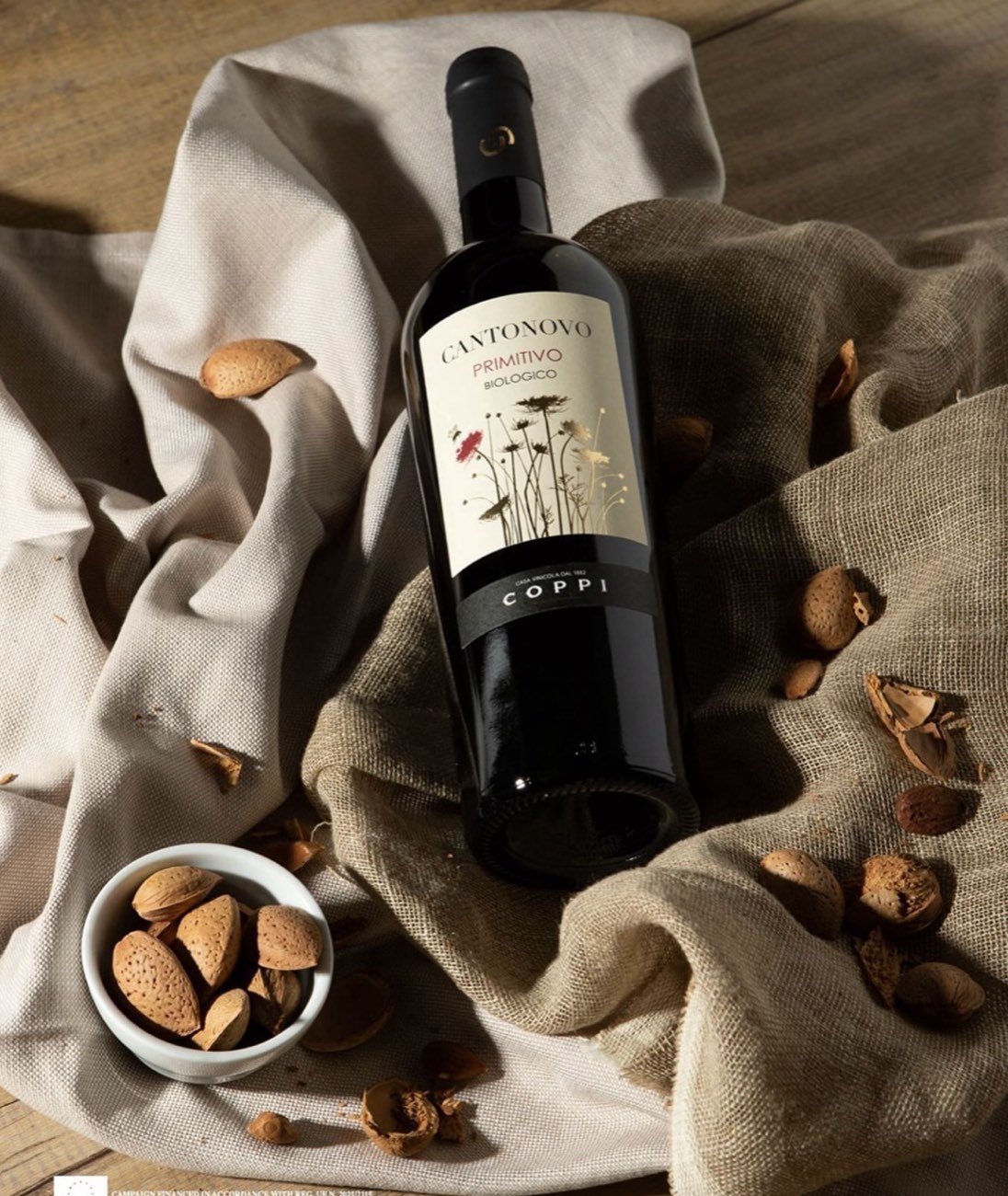 A dark Coppi bottle on rumpled linen with a bowl of almonds