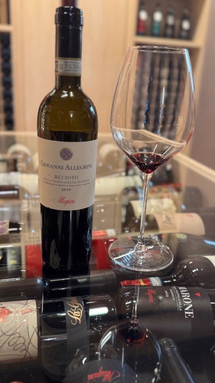 A bottle and a poured glass of red wine on an enoteca counter