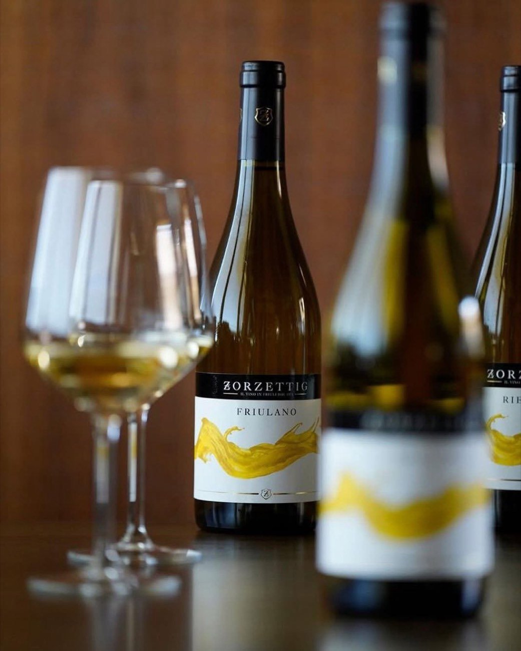 Three Zorzettig white wine bottles beside a filled glass